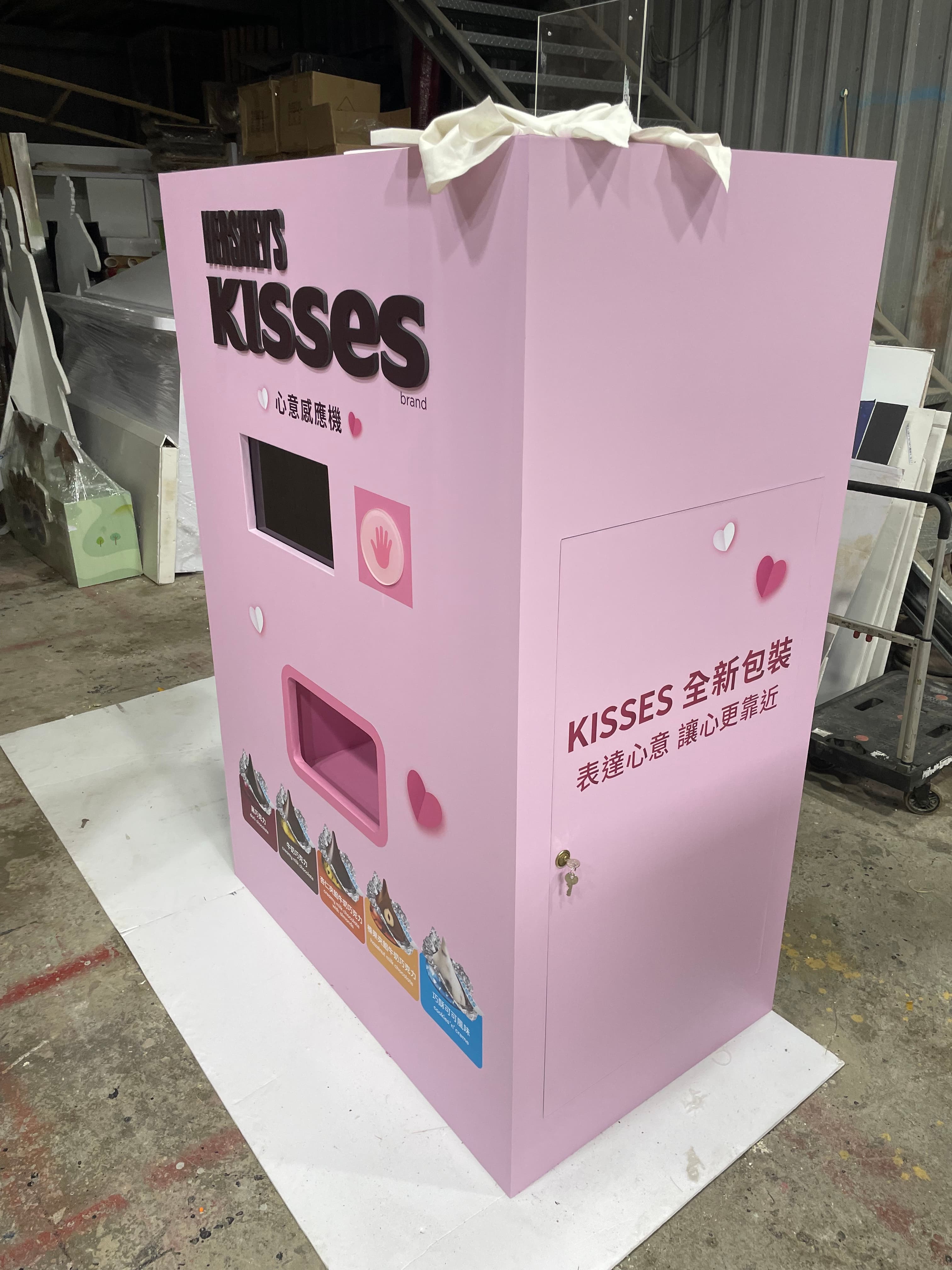 粉紅色 KISSES 心意感應機，設有觸控畫面、手掌感應區與取貨口
